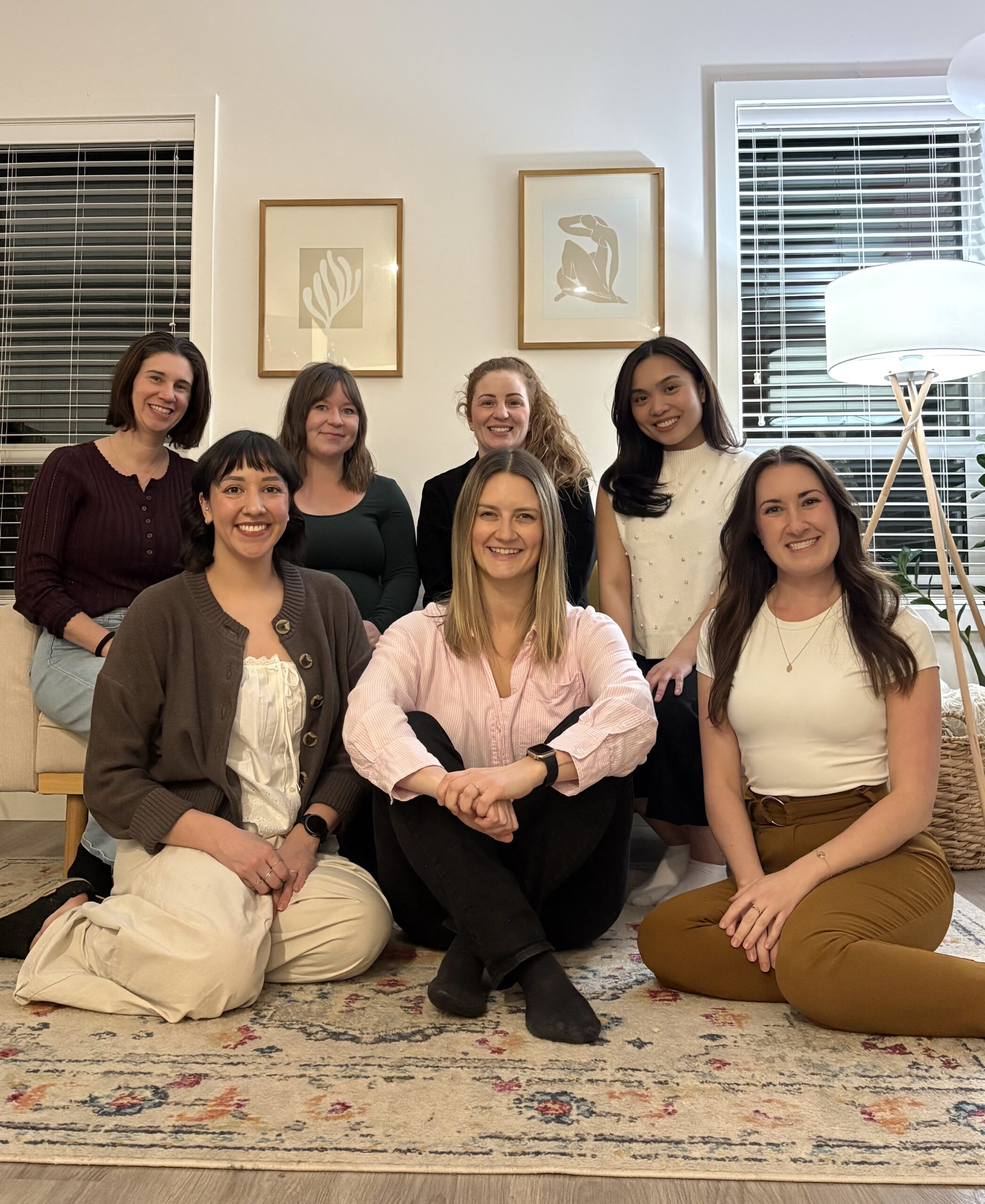 The seven-person team of Wordplay Therapy, all women, are sitting and smiling together in a warm, inviting office setting.